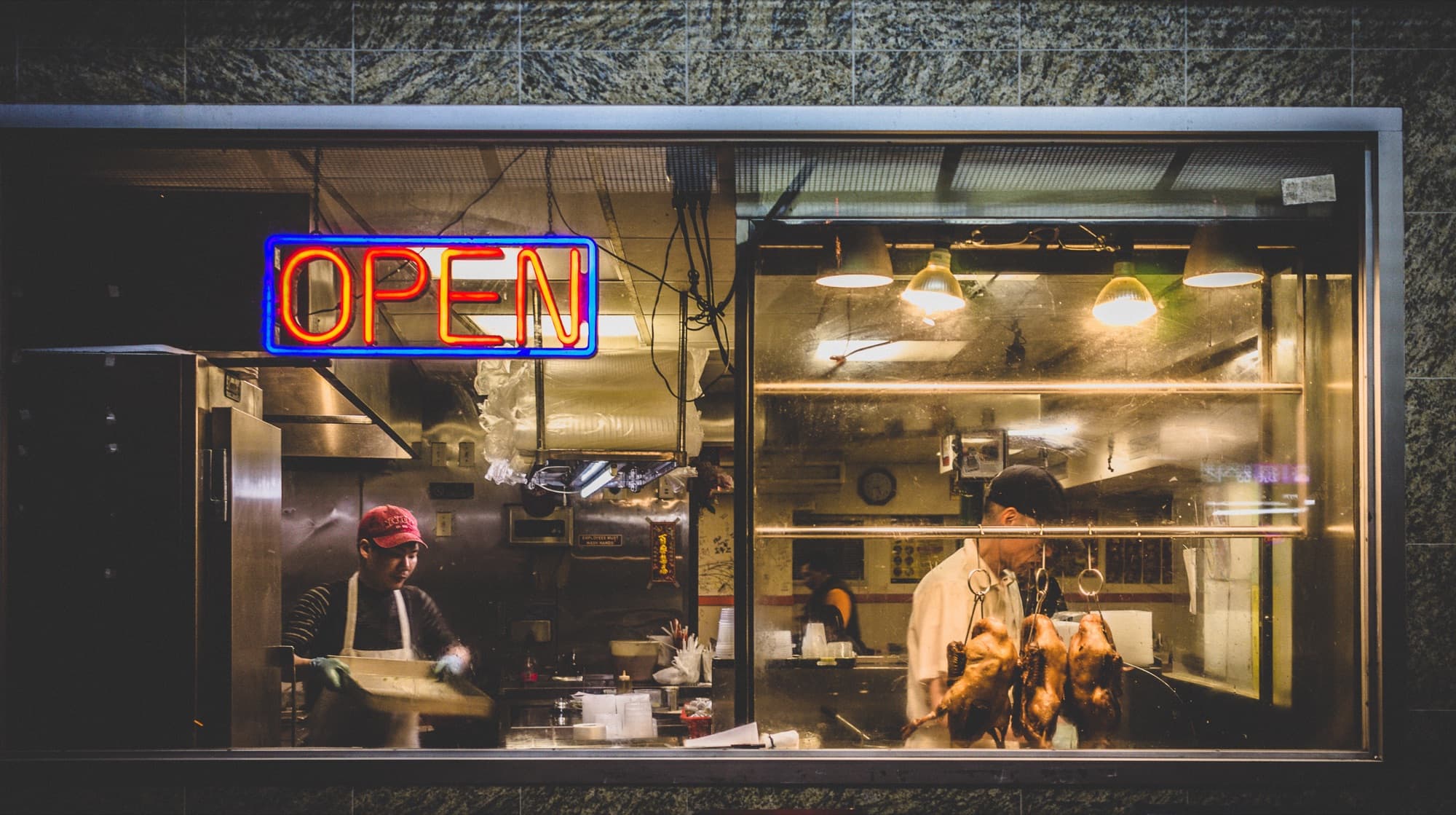 A restaurant storefront at night with an open sign in the window